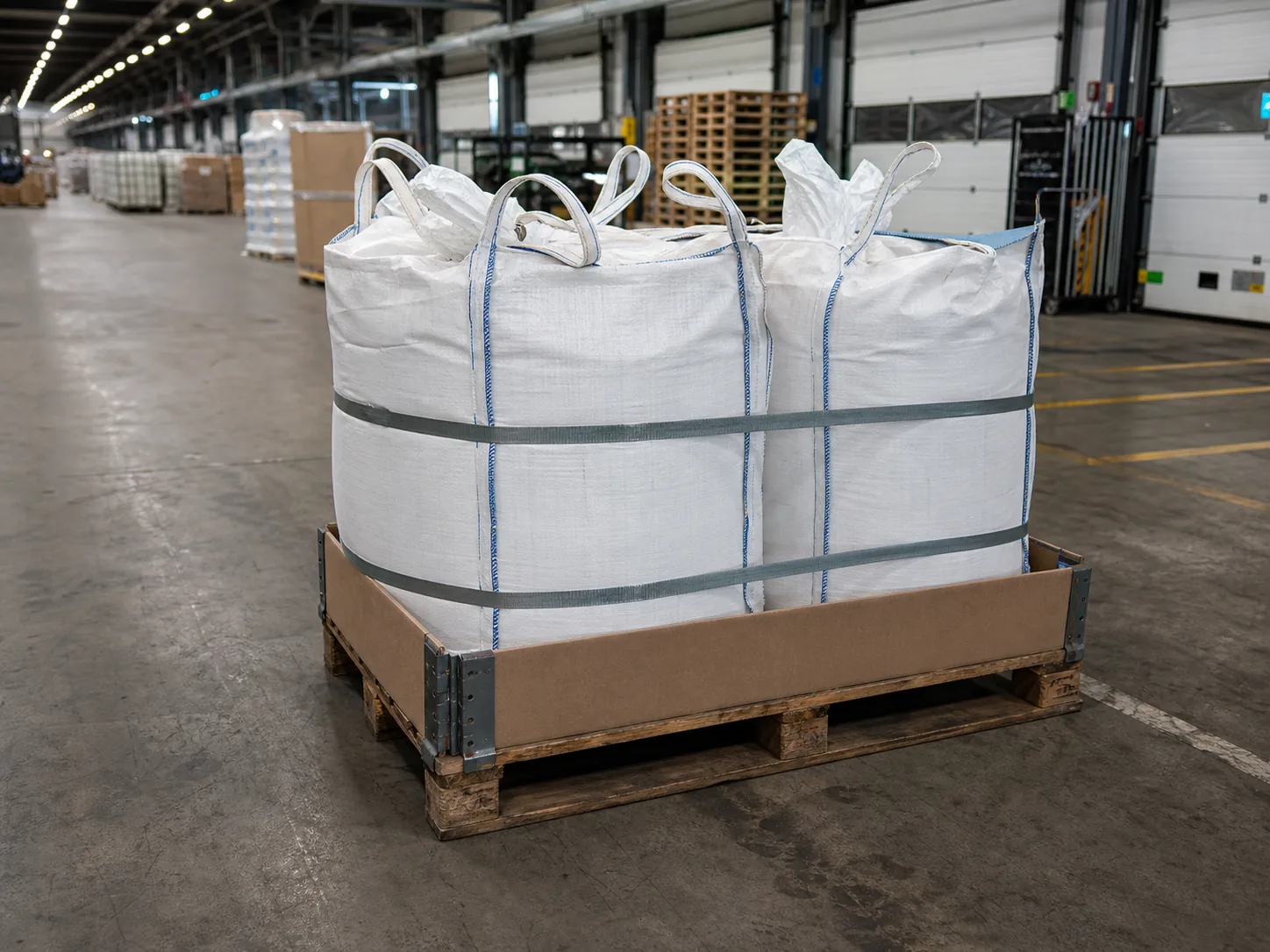 Zwei weiße Big Bags mit Palettenrahmen und Gurten in einer Umschlaghalle