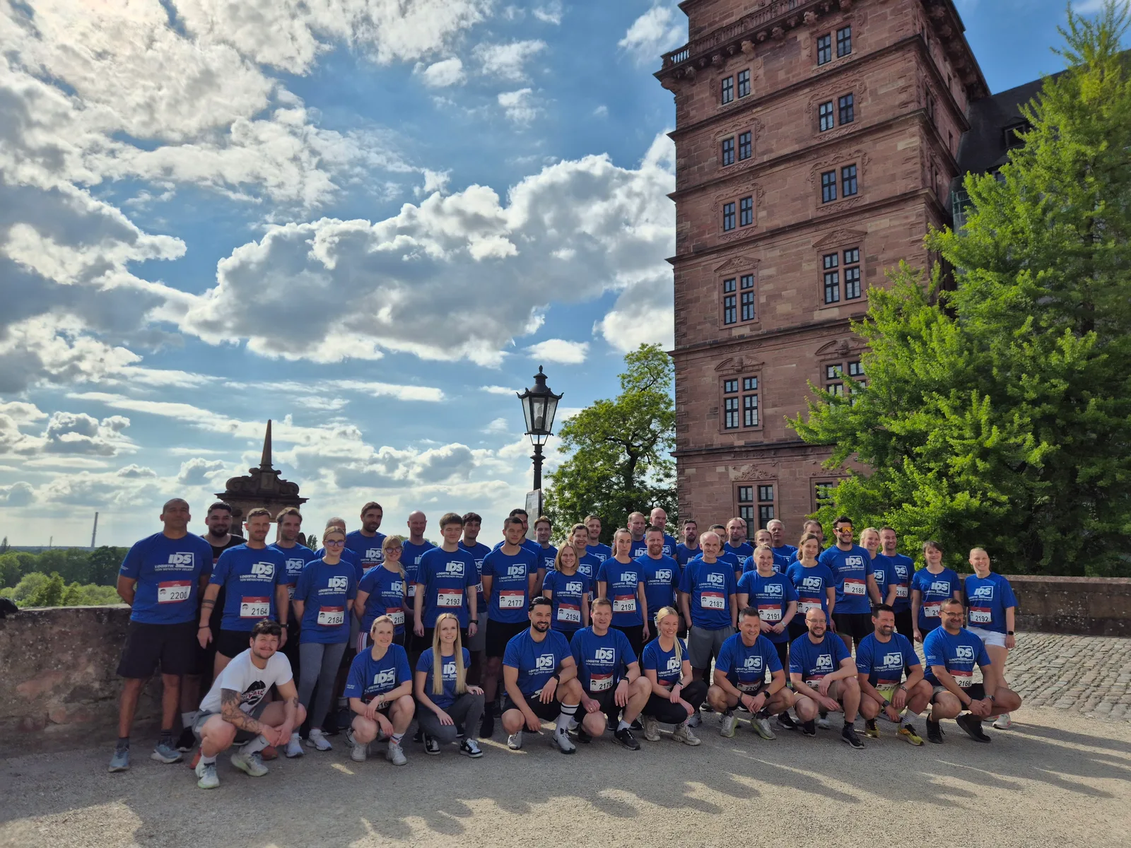 Rund 45 Kolleginnen und Kollegen aus dem IDS-Netzwerk in blauen Team-Shirts mit Startnummern vor dem Schloss in Aschaffenburg